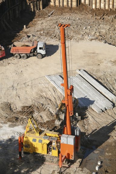 Construction site with a large orange crane and yellow machinery among dirt and materials.